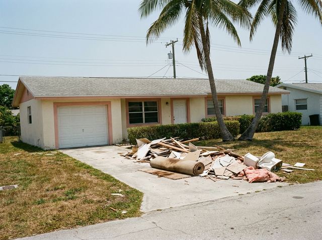 Renovation debris piled on a driveway: drywall, lumber, tile and a rolled-up carpet