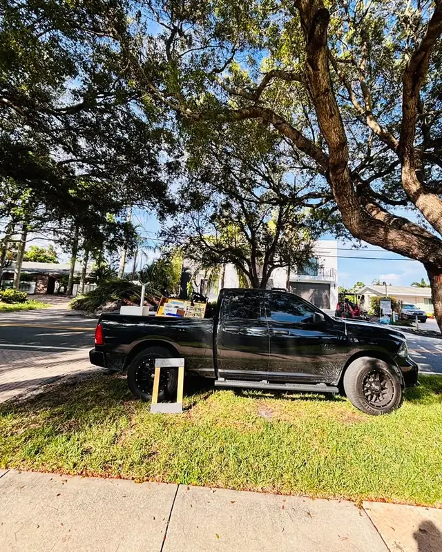 Eddy's black pickup parked under a tree, bed loaded with a whiteboard and furniture